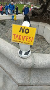 Penguin figure on edge of fountain wearing sign: "No tariffs! Hands off my herring!"