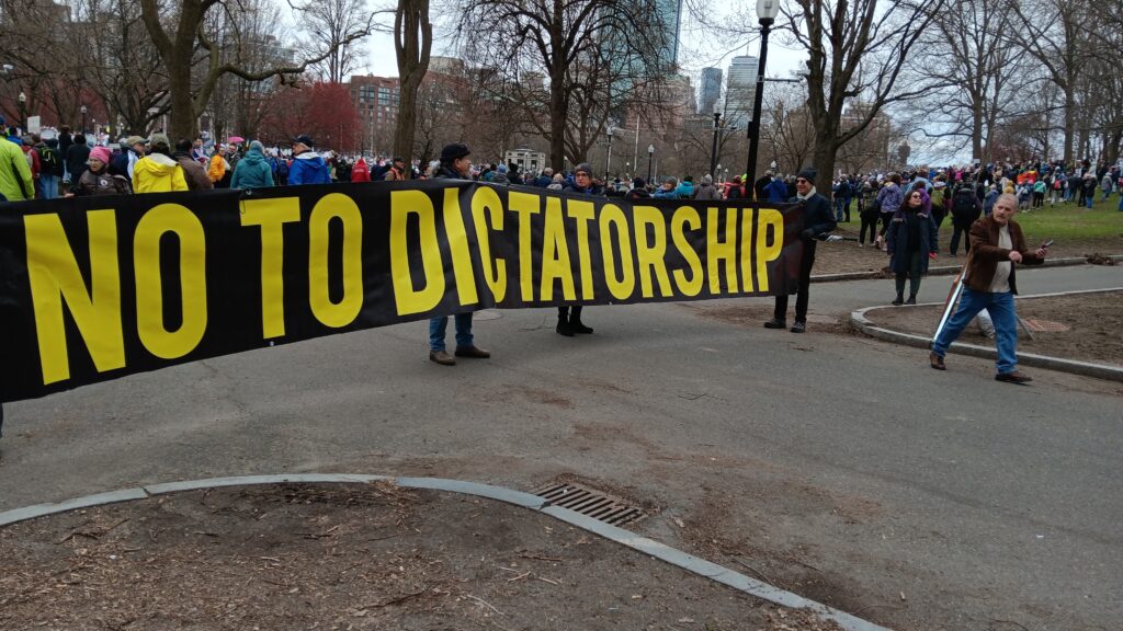 People in Boston Common holding a very large sign reading "NO TO DICTATORSHIP"