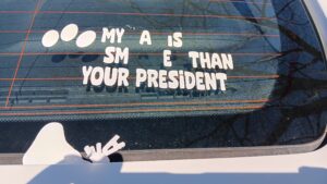 Windshield sticker with missing letters indicated by brackets: "My [c]a[t] is sm[art]e[r] than your president"